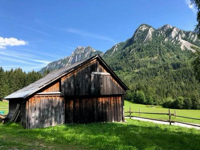 A weathered timber hay barn in a green meadow below the peaks